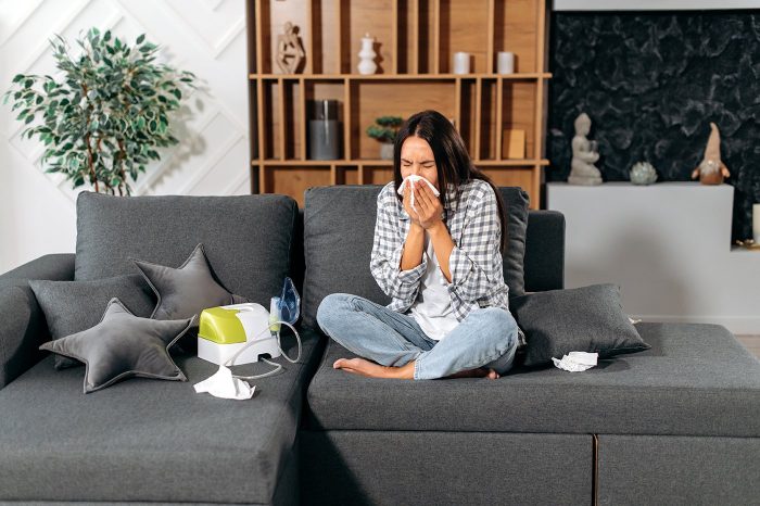 sick woman blowing her nose sitting on couch at home sick woman blowing her nose sitting on couch at home